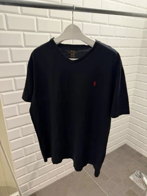 Svart t-shirt från Polo Ralph Lauren - Snygg svart t-shirt från Polo Ralph Lauren med klassisk röd logga broderad på bröstet. T-shirten har v-ringning och är tillverkad i mjuk bomull. Enkel och stilren design som passar till det mesta.
