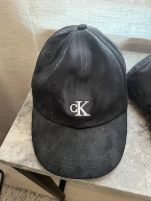Calvin klein keps  - Keps från Calvin Klein i storlek 8-14 år, men passar även äldre. Är justerbar där bak. Aldrig använd, bara stått i en hylla så är dammig.