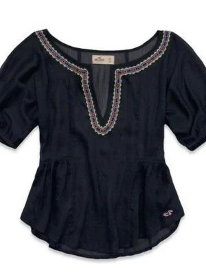 Hollister y2K  blus med broderad kant stl XS-S - Mörkblå blus från Hollister med broderad kant i lila, rosa och grönt runt den djupa V-ringningen. Blusen har puffiga korta ärmar och är gjord i ett tunt, transparent material som ger en luftig känsla. Liten broderad logga nertill. Använd 1-2 gånger bara.