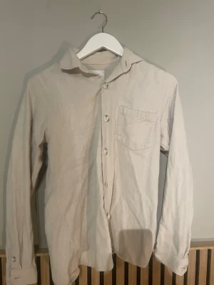Beige skjorta med bröstficka - Stilren och snygg overshirt som är gjord av ett mjukt och lent material. Overshirten har en ficka på bröstet och funkar till det mesta. Pris kan diskuteras.
