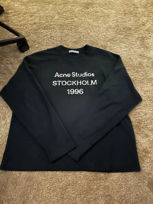 Navy långärmad topp Acne Studios - Svart långärmad topp från Acne Studios med tryck 'Acne Studios STOCKHOLM 1996' på bröstet. Klassisk rak passform och rund halsringning. Tillverkad i mjuk bomull som känns skön mot huden.