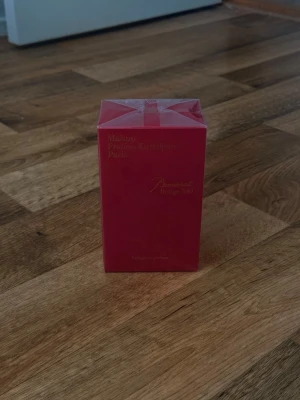 Maison Francis Kurkdjian Baccarat Rouge 540 Eau de Parfum, 70 ml - Lyxig parfym i en elegant röd kartong med gulddetaljer och stilren design. Förpackningen har ett exklusivt tryck med ett husmotiv på sidan och text i guld på framsidan. Perfekt för dig som gillar exklusiva dofter och snygg design på parfymflaskan.