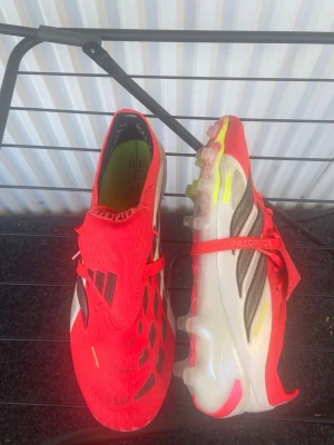Adidas Predator röda fotbollsskor - Säljer ett par Adidas Predator fotbollsskor i rött med svarta och vita detaljer. Skorna har snörning, låg profil och dobbar för bra grepp på planen. Ovandelen är i syntetmaterial och designen är modern med coola mönster och logga på tån. Skorna är använda fåtal gånger. Nypris ca 3000kr. Storlek 44 2/3.