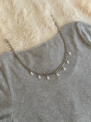 Silverfärgat halsband med pärldroppar - Snyggt halsband i silverfärgad rostfritt med kedjedesign och sju droppformade pärlor som hänger längs kedjan. Perfekt för att ge en cool touch till din outfit. Passar till många olika stilar och är lätt att matcha med andra accessoarer.