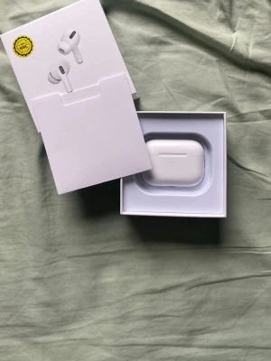 AirPods gen 2 pro - Säljer ett par vita trådlösa in-ear hörlurar med laddningsetui. Hörlurarna har en stilren och kompakt design med silikonproppar för bra passform. Perfekta för musik, poddar och samtal på språng. Laddas enkelt i det medföljande etuiet.