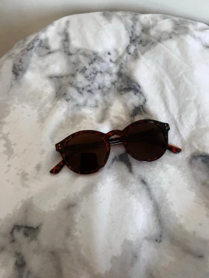 Runda solglasögon i leopardmönster - Snygga runda solglasögon med leopardmönstrad båge och mörka linser. Perfekta för att ge din look en trendig touch. Bågarna har en klassisk form och passar till många olika stilar.