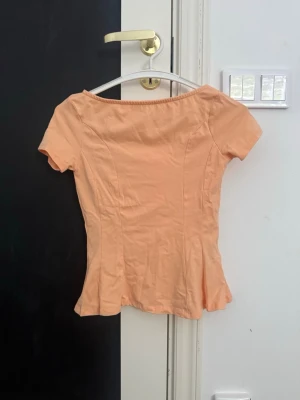 Ljus orange kortärmad topp - Snygg ljus orange topp med korta ärmar och lätt utsvängd nederkant. Toppen har en enkel, figurnära passform och är tillverkad i ett mjukt material som känns bekvämt mot huden. Perfekt för en fräsch och somrig look.