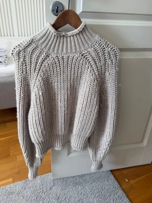Beige chunky stickad tröja H&M - Chunky stickad tröja från H&M i beige färg. Tröjan har hög krage, breda ribbstickade muddar och ett grovt stickat mönster. Perfekt för kalla dagar och superenkel att styla med jeans eller kjol.