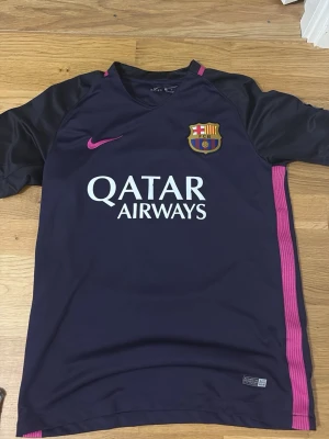 Barça Neymar Jr matchtröja lila/rosa - Säljer en FC Barcelona matchtröja i mörklila med rosa detaljer och tryck. Tröjan har Neymar Jr och nummer 11 på ryggen, samt Qatar Airways och UNICEF-logga. Officiell klubbmärke på bröstet och Nike-logga. Perfekt för fotbollsfans!