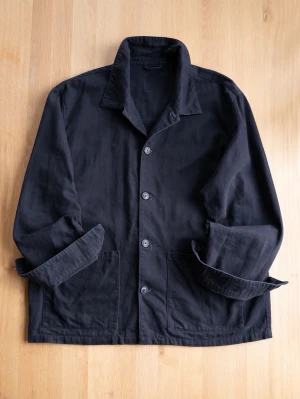 Black Chore Jacket, size XL - Stilren svart overshirt med klassisk krage och knäppning framtill. Jackan har två stora framfickor och är tillverkad i ett kraftigare bomullstyg. Perfekt för lager-på-lager och enkel att matcha med olika outfits.