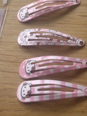Söta rosa Hello Kitty hårspännen - Fyra hårspännen i metall med Hello Kitty-motiv i olika rosa nyanser och mönster som prickar och ränder. Perfekta för att piffa upp frisyren med en gullig och lekfull touch. Motiv i vitt, rosa och rött med klassiska Hello Kitty-detaljer.