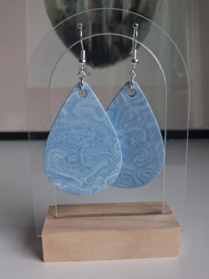 Blå droppformade örhängen mellan jesmonite  - Snygga örhängen i droppformad design med marmorerat mönster i ljusblått och lite vitt. De har silvriga krokar som är nickelfria och är tillverkade i jesmonite. Längd på droppen är 5cm långa. Blir en fin touch till outfiten.
