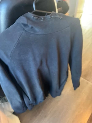 Svart hoodie från SDC i storlek M - Svart hoodie från SDC i storlek M. Klassisk modell med huva och dragsko, tillverkad i mjukt material. Perfekt för en avslappnad och stilren look. Passar bra till jeans eller joggers.
