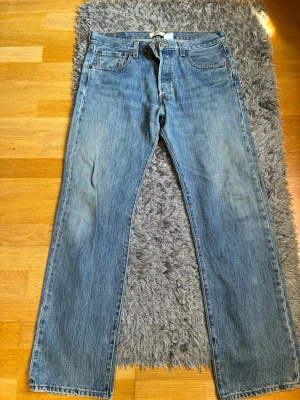 Blå raka jeans från Levi's - Klassiska blå jeans från Levi's med rak passform och fem fickor. Jeansen har en ljus tvätt och tydliga sömmar, samt den ikoniska röda Levi's-lappen på bakfickan. Tillverkade i slitstark denim som ger en tidlös look. Passar både herr och unisex. 