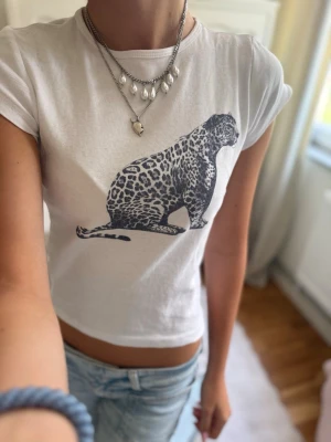 Vit leopardmönstrad t-shirt Subdued - Säljer en vit kortärmad t-shirt från Subdued med ett stort leopardtryck framtill. T-shirten har en tight passform och är gjord i mjuk bomull, perfekt till jeans eller kjol för en cool och avslappnad look.