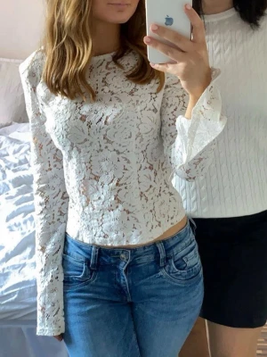 Vit spetsblus med lång ärm - Säljer en superfin vit blus i spets med lång ärm och rund hals. Blusen har ett blommigt spetsmönster och är lätt genomskinlig, vilket ger en trendig och elegant look. Passar perfekt till jeans eller kjol för en snygg outfit. Storlek 38 men passar även 36. 