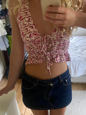 Rosa och vit blommig halterneck topp - Supersöt halterneck topp i vitt och rosa med blommigt mönster. Toppen har snörning framtill och volangkant nedtill. Perfekt för varma dagar och ger en riktigt somrig vibe.