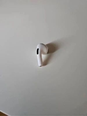 Air pod 3 höger öra - Säljer en vit trådlös in-ear hörlur med stilren och kompakt design. Hörluren har en slimmad form och svarta detaljer på utsidan. Perfekt för dig som vill ha smidig musikupplevelse utan sladdar. Priset kan Diskuterad