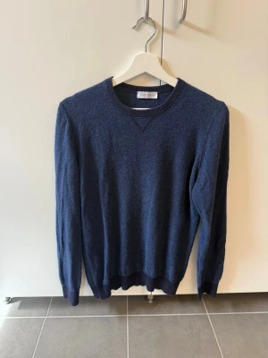 Mörkblå stickad tröja Gran Sasso, stl 48/M - Snygg mörkblå stickad tröja från Gran Sasso med rund halsringning och ribbade muddar vid ärmslut och nederkant. Tillverkad i Italien och har en klassisk, enkel design som passar perfekt till jeans eller chinos.