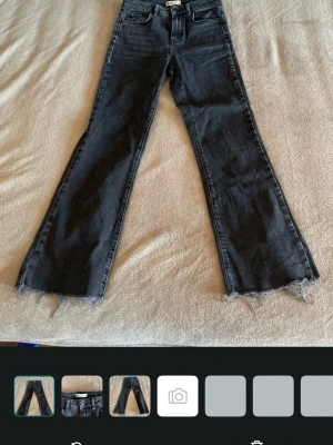 Svarta bootcut jeans med rå kant - Säljer ett par svarta bootcut jeans från Perfect Jeans i storlek 34. Jeansen har råa, fransiga benslut och klassisk femficksmodell. Materialet är denim med en tvättad look och de har hällor för skärp. Perfekta för en trendig och avslappnad stil.