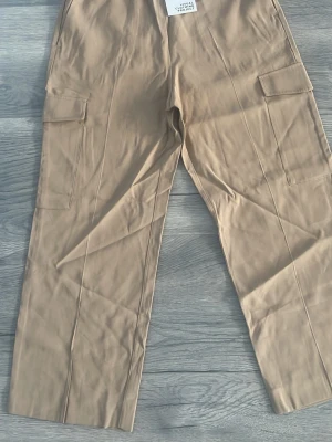 Beige cargobyxor med raka ben - Snygga beige cargobyxor med raka ben och stora fickor på sidorna. Byxorna har en avslappnad passform och är perfekta för en casual look. Tillverkade i ett mjukt och slitstarkt material som känns bekvämt hela dagen.