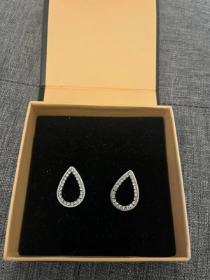 Silvriga droppformade örhängen - Snygga silvriga örhängen i droppform med gnistrande stenar runt hela kanten. Perfekta för dig som gillar stilrena och eleganta accessoarer. (Obs, kommer inte i asken)🥰