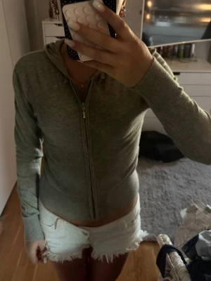 Grå zip hoodie med huva - Säljer en grå hoodie med dragkedja och huva. Modellen är figurnära med långa ärmar och ribbade muddar vid ärmslut och nederkant. Perfekt till jeans eller shorts för en avslappnad look. Materialet känns mjukt och stretchigt.