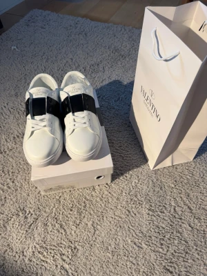 Valentino opens  - Valentino Open Sneakers – Vita och svarta   Säljer ett par helt nya och oanvända Valentino Open sneakers i vitt😍. Skorna är i perfekt skick och har aldrig blivit använda 👌. Passar ungefär som en storlek 42, så tänk på det vid köp.  Originaltillbehör ingår:  * Original Valentino-box * Originalpapper * Valentino-påse  Ett riktigt snyggt och stilrent par sneakers som passar till både vardag och finare outfits. 