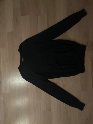 Mörkgrön stickad tröja Polo Ralph Lauren - Mörkgrön stickad tröja från Polo Ralph Lauren i slim fit-modell. Tillverkad av 100% maskintvättbar merinoull. Klassisk rund halsringning och långa ärmar, perfekt för en stilren och bekväm look.