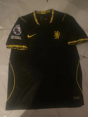 Chelsea FC svart matchtröja Palmer 10 - Snygg svart Chelsea FC matchtröja från Nike med gula detaljer och klubbmärke på bröstet. Nummer 10 och namnet Palmer på ryggen. Premier League-märke och 'No room for racism' på ärmarna. Tillverkad i lätt och ventilerande material, perfekt för fotbollsträning.