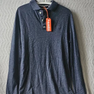 Mörkblå långärmad skjorta Superdry - Snygg mörkblå långärmad skjorta från Superdry med klassisk krage och knappar framtill. Skjortan har en diskret logga på bröstet och är tillverkad i ett mjukt material som passar perfekt till många olika stilar.