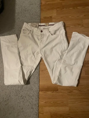 Vita tramarossa jeans - Säljer ett par vita jeans med rak passform och klassisk femficksdesign. Jeansen har bälteshällor och knappgylf. Perfekta för dig som vill ha en clean och stilren look. Materialet ser ut att vara bomull med lite stretch. Waisted sitter som 28-29