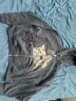  Enfants Riches Déprimés hoodie - Storlek S.Säljer en svart hoodie med dragkedja från Enfants Riches Déprimés. På framsidan finns ett stort, edgy tryck i beige av ett grisansikte och en person med hatt och solglasögon. Hoodien har huva och känguruficka. Materialet är mjukt och känns riktigt skönt.