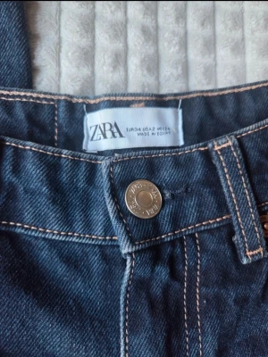 Mörkblå raka jeans från ZARA - Säljer ett par mörkblå jeans från ZARA med raka ben och råa, fransiga benslut. Klassisk femficksmodell med kontrastsömmar och hög midja. Perfekta för en avslappnad och trendig look. Midja: 32,5 cm, längd 113 cm. Skriv gärna om fler bilder eller mått önskas. 🫶