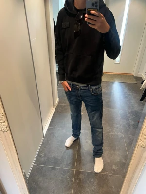 Alpha industrie hoodie  - Säljer en svart hoodie med huva och en patch på bröstet. Hoodien har en ficka på ärmen med dragkedja och klassisk känguruficka framtill. Perfekt för dig som gillar en enkel men ändå cool stil. Materialet känns mjukt och bekvämt.