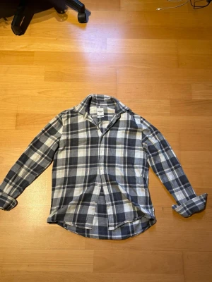 Rutig skjorta från Dobber  - Säljer en klassisk rutig skjorta från Dobber i mjuk bomull. Skjortan har lång ärm, knappar framtill och en avslappnad passform. Färgkombinationen är svart, vit och grå, perfekt för en chill och stilren look. Priset är inte hugget i sten🙌