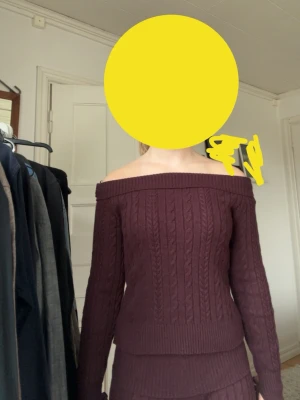 Vinröd off shoulder stickad tröja  - Säljer en vinröd stickad tröja med off shoulder-modell och kabelstickat mönster. Tröjan har långa ärmar med tumhål och bred ribbad kant vid midjan. Perfekt för dig som gillar en trendig och mysig stil.