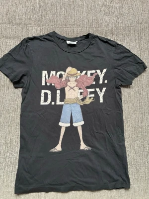 Svart One Piece t-shirt Monkey D. Luffy - Svart t-shirt med stort tryck av Monkey D. Luffy från One Piece på framsidan. T-shirten har rund hals och korta ärmar. Perfekt för dig som älskar anime och vill ha en stilren men cool look.