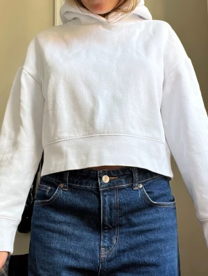 Vit croppad hoodie - Säljer en vit croppad hoodie med huva och långa ärmar. Hoodien har en enkel och clean design utan tryck eller logga, och är gjord i ett mjukt sweatshirtmaterial som känns skönt mot huden. Perfekt till jeans eller mjukisbyxor.