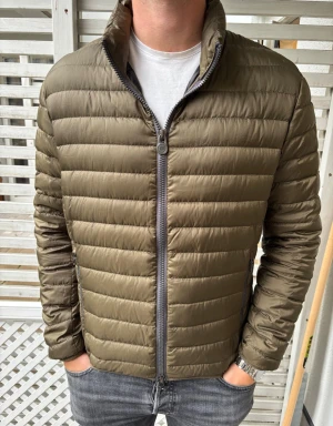 Olivgrön pufferjacka från Colmar - Snygg olivgrön pufferjacka från Colmar med quiltad design och hög krage. Jackan har dragkedja framtill, två sidofickor med dragkedja och Colmar-logga på vänster ärm. Tillverkad i lätt, glansigt material som håller värmen utan att kännas tung.