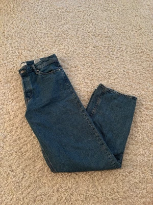 Blå raka jeans i klassisk modell - Ett par blå jeans i klassisk rak modell med fem fickor och knappgylf. Jeansen har en tidlös tvätt och är tillverkade i denim med tydlig struktur. Passar perfekt till en avslappnad stil och är lätta att matcha med olika plagg.