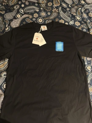 Svart t-shirt från Casablanca - Snygg svart t-shirt från Casablanca med tryck i blått och vitt på bröstet. Klassisk rund hals och korta ärmar. Tillverkad i mjuk bomull för en skön känsla. Perfekt för dig som gillar stilrena plagg med en twist. 