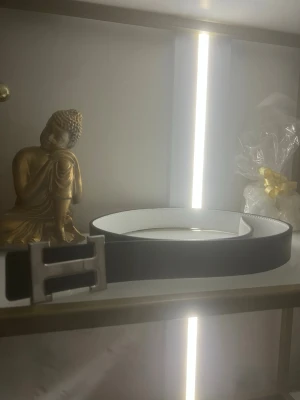 Svart bälte H med silverfärgat spänne 120cm - Snyggt svart bälte med ett stort, silverfärgat H-format spänne. Bältet har en stilren och enkel design med vit insida, perfekt för att lyfta vilken outfit som helst.