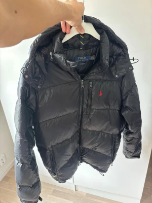 Svart glänsande Ralph lauren vinter dunjacka herr M - Svart glänsande eftertraktad och populär ursnygg vinter dunjacka av högsta kvalité och storlek M säljes. Inga hål eller fläckar och superfint skick så gott som ny! Perfekta vinterjackan och superfint topp skick. Tveka inte vid minsta fråga eller fundering pris ej hugget i sten