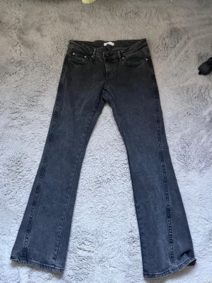 Svarta bootcut med vintagekänsla - Säljer ett par svarta jeans från Gina Tricot i storlek M med bootcut passform och klassisk femficksdesign. Jeansen har en tvättad vintage-look och är tillverkade i ett robust denimtyg. Perfekta för dig som gillar en avslappnad och tidlös stil. De är helt nya och aldrig använda. 