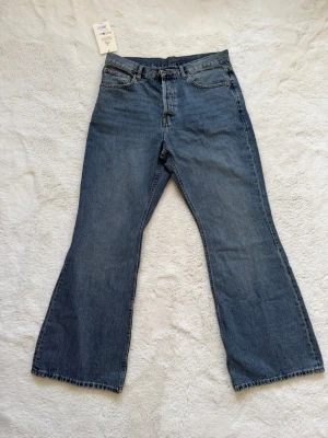 Blåa bootcut jeans - Säljer ett par klassiska blåa bootcut jeans med hög midja och fem fickor. Jeansen har en rak passform upptill och vida ben från knät och ner. Tillverkade i kraftigt denimtyg som ger en snygg vintagekänsla. Perfekta för dig som gillar retrostil!