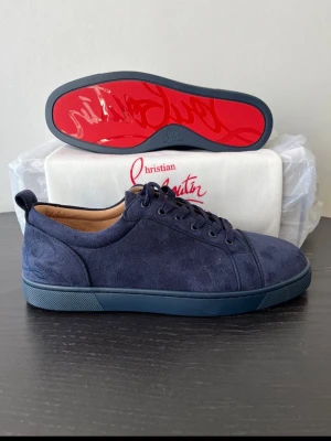 Marinblå mockasneakers Christian Louboutin - Säljer ett par marinblå sneakers från Christian Louboutin i mjuk mocka med klassisk röd sula och ton-i-ton broderad logga på hälen. Skorna har snörning och en stilren, låg profil som passar till många olika looks. Allt OG medföljer förutom OG box