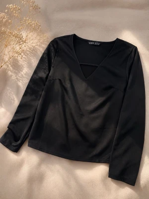 Svart långärmad topp med v-ringning - Snygg svart långärmad topp med v-ringning och en dekorativ rem över bröstet. Enkel och stilren design som passar till många olika outfits. Tillverkad i ett mjukt och stretchigt material för skön passform.