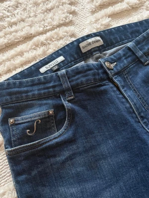 Mörkblå jeans från Sacre Denim - Snygga mörkblå jeans från Sacre Denim i rak modell med klassiska fem fickor och diskret logga på myntfickan. Jeansen har en lätt tvättad look och är tillverkade i ett mjukt denimtyg som sitter skönt hela dagen.