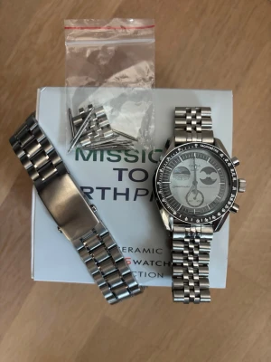 Moddad Omega x Swatch Mission to Earthphase - Detta är en omega x swatch Moonswatch mission to earthphase som är modifierad med en metallboett och metallarmband inspirerat av omega speedmaster. Perfekt för dig som vill ha en moonswatch men tycker att det känns fjantigt med en plastklocka eller drömmer om en speedmaster. Den har en skön tyngd och är byggd på korrekt sätt med delar av hög kvalitet. 42mm stor. Låda, original boett och extra länkar följer med. Skriv om du har några frågor! 